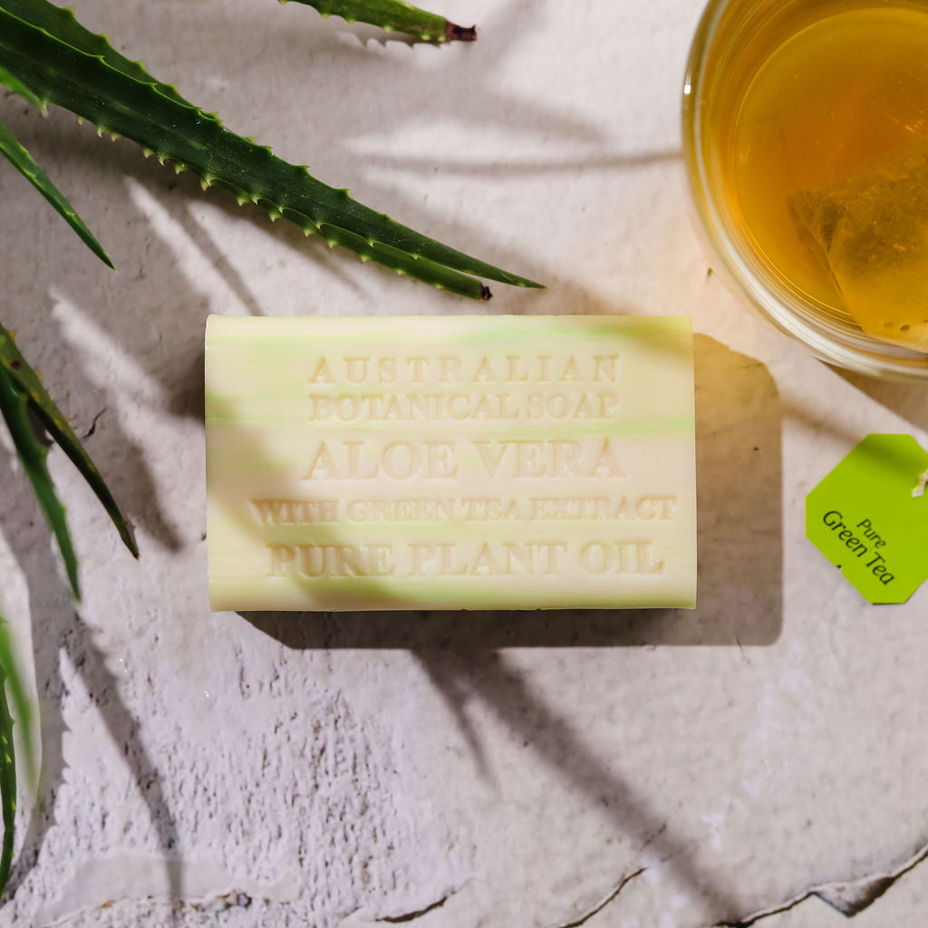 Bar of Australian botanical soap with aloe vera and green tea extract on a light surface with aloe vera leaves.