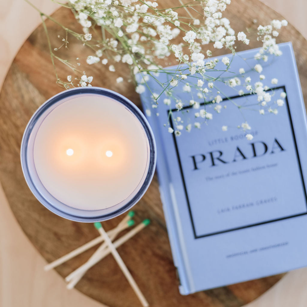 Candle, matches, and a book titled 'Prada' on a wooden surface.