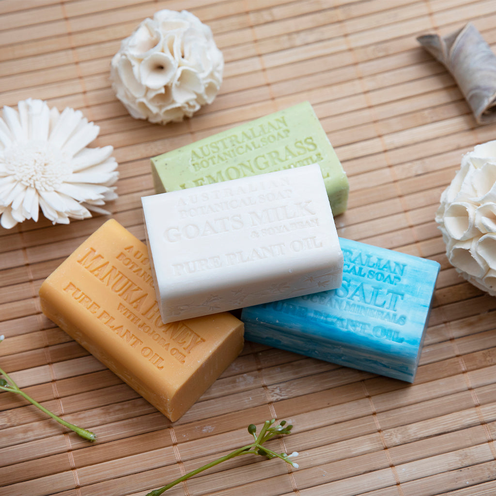 Four bars of soap in different colors on a wooden surface with flowers around.