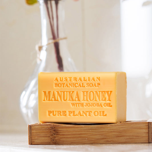 Bar of Australian Botanical Soap with Manuka Honey on a wooden block with a blurred vase in the background.