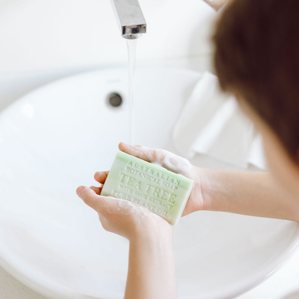 Person holding a bar of soap over a sink with water running.