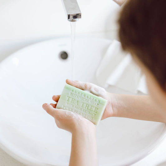 Person holding a bar of soap over a sink with water running.