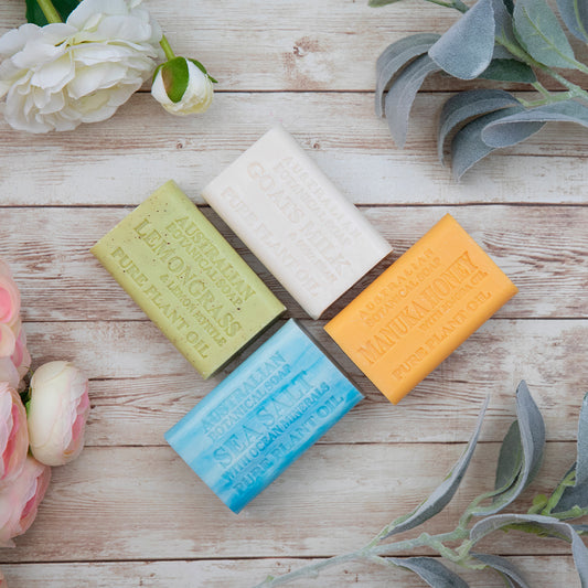 Four bars of soap in different colors on a wooden surface with flowers and leaves.
