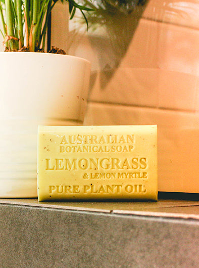 Bar of Australian Botanical Soap with lemongrass and lemon myrtle scent on a surface with a plant in the background.