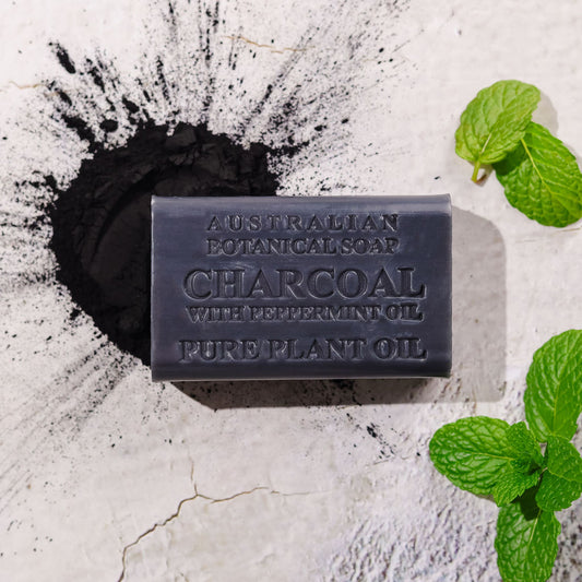 Activated charcoal with peppermint soap bar on a textured white background with mint leaves and charcoal powder