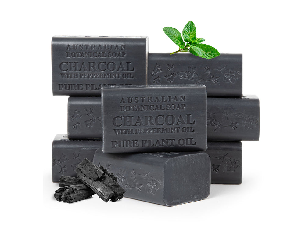 Stack of charcoal soap bars with peppermint leaves on a white background