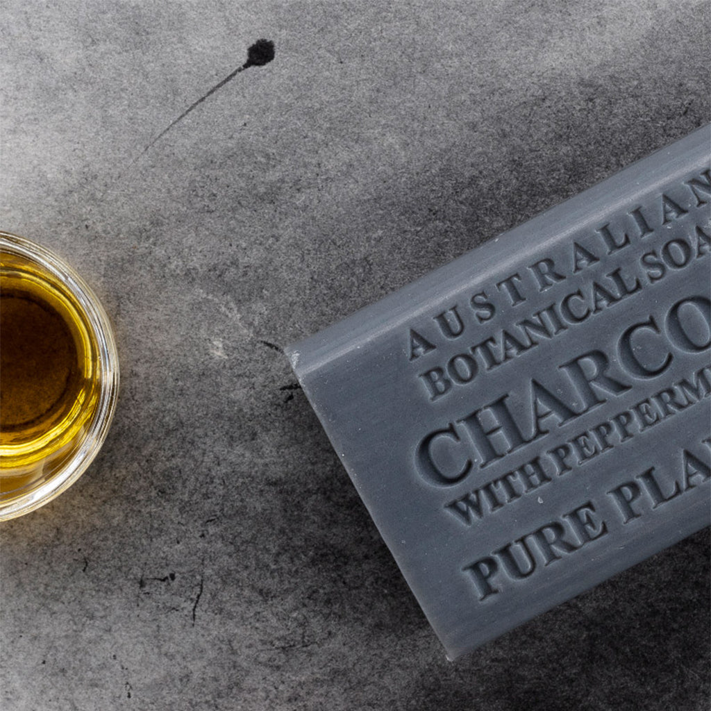 Bar of Australian Botanical Soap with Peppermint and Charcoal on a gray surface next to a glass of liquid.