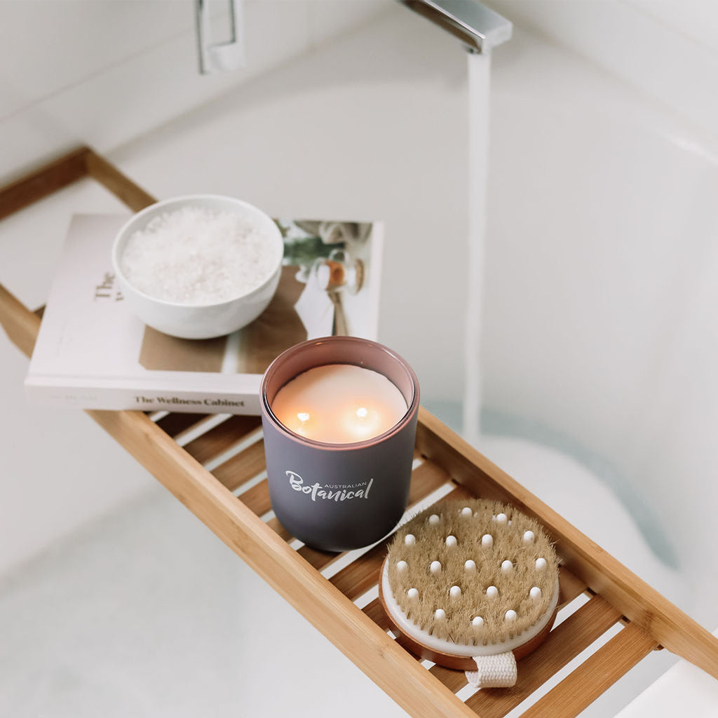 Candle in a decorative tray with bath items on a bathtub ledge