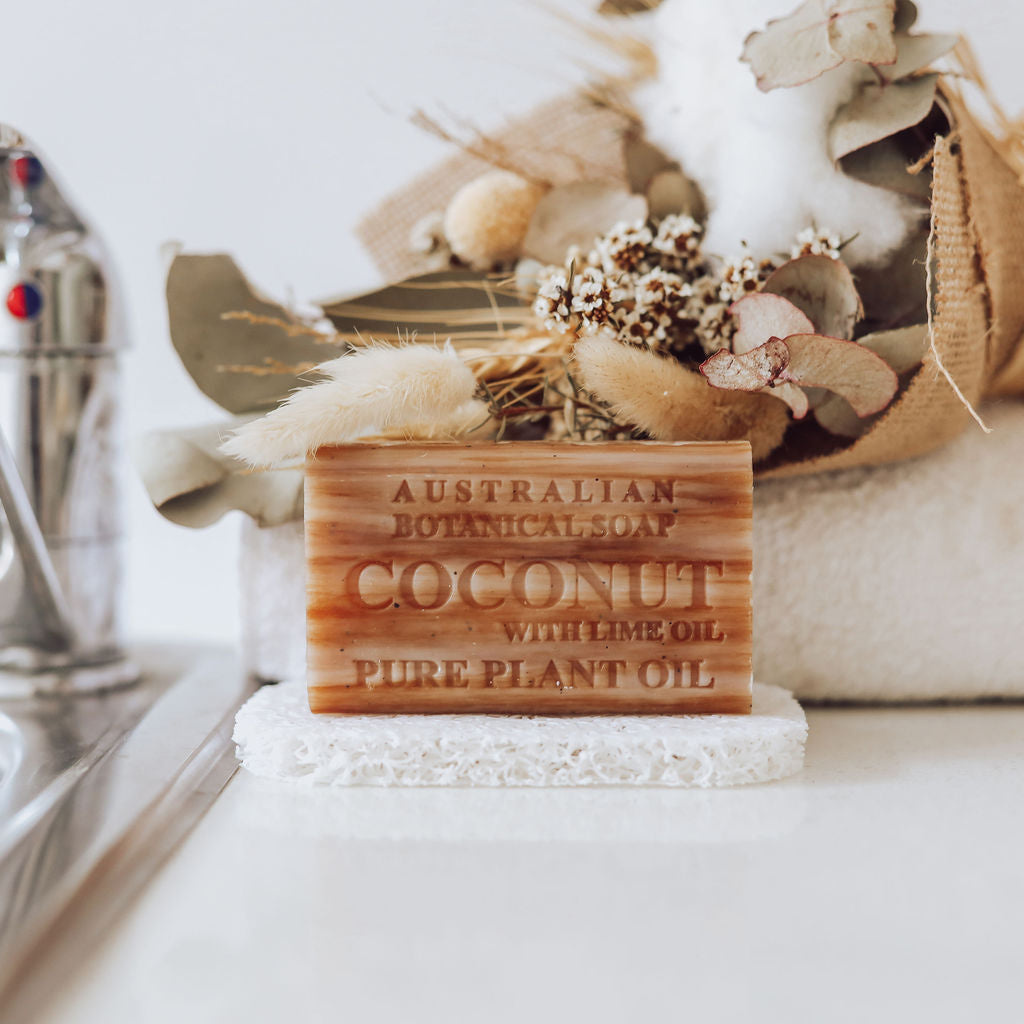 Bar of Australian Botanical Soap on a white surface with flowers in the background