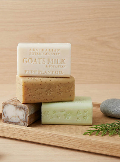 Four bars of Australian botanical soap on a wooden surface with a stone and greenery.