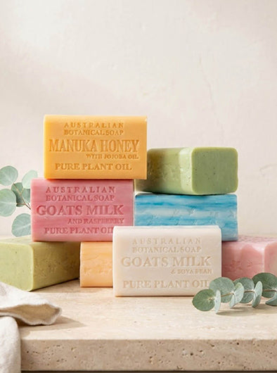 Stack of colorful Australian Botanical Soap bars on a light surface with eucalyptus leaves.