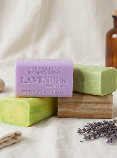 Two bars of Australian Botanical Soap with lavender essential oil on a wooden block, surrounded by lavender flowers.