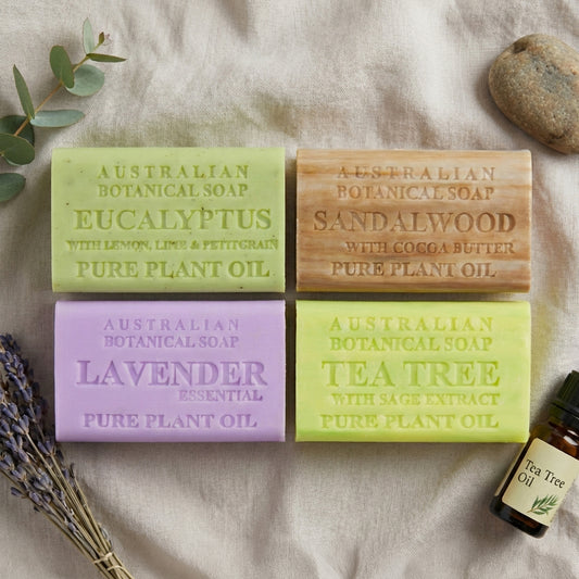 Four Australian Botanical Soap bars with labels on a textured surface with lavender and a stone.