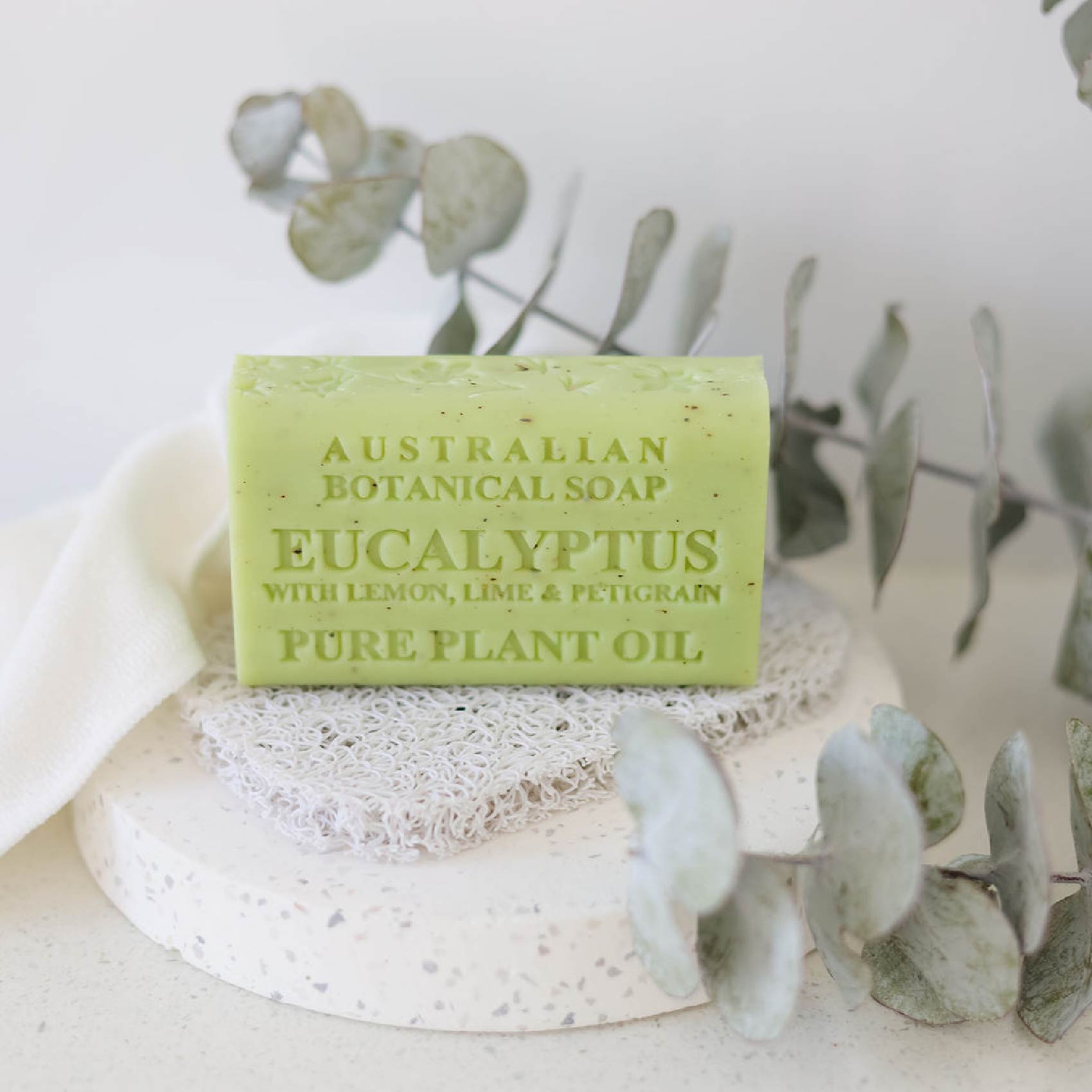 Green bar of Australian Botanical Soap with Eucalyptus scent on a white surface with eucalyptus leaves.