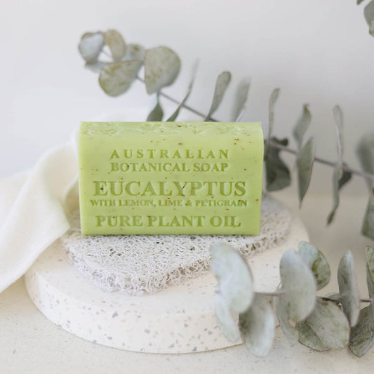 Green bar of Australian Botanical Soap with Eucalyptus scent on a white surface with eucalyptus leaves.