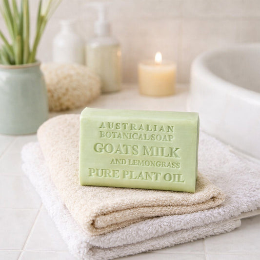 Bar of Australian Botanical Soap with goat's milk and lemongrass on a towel with a candle and plant in the background.