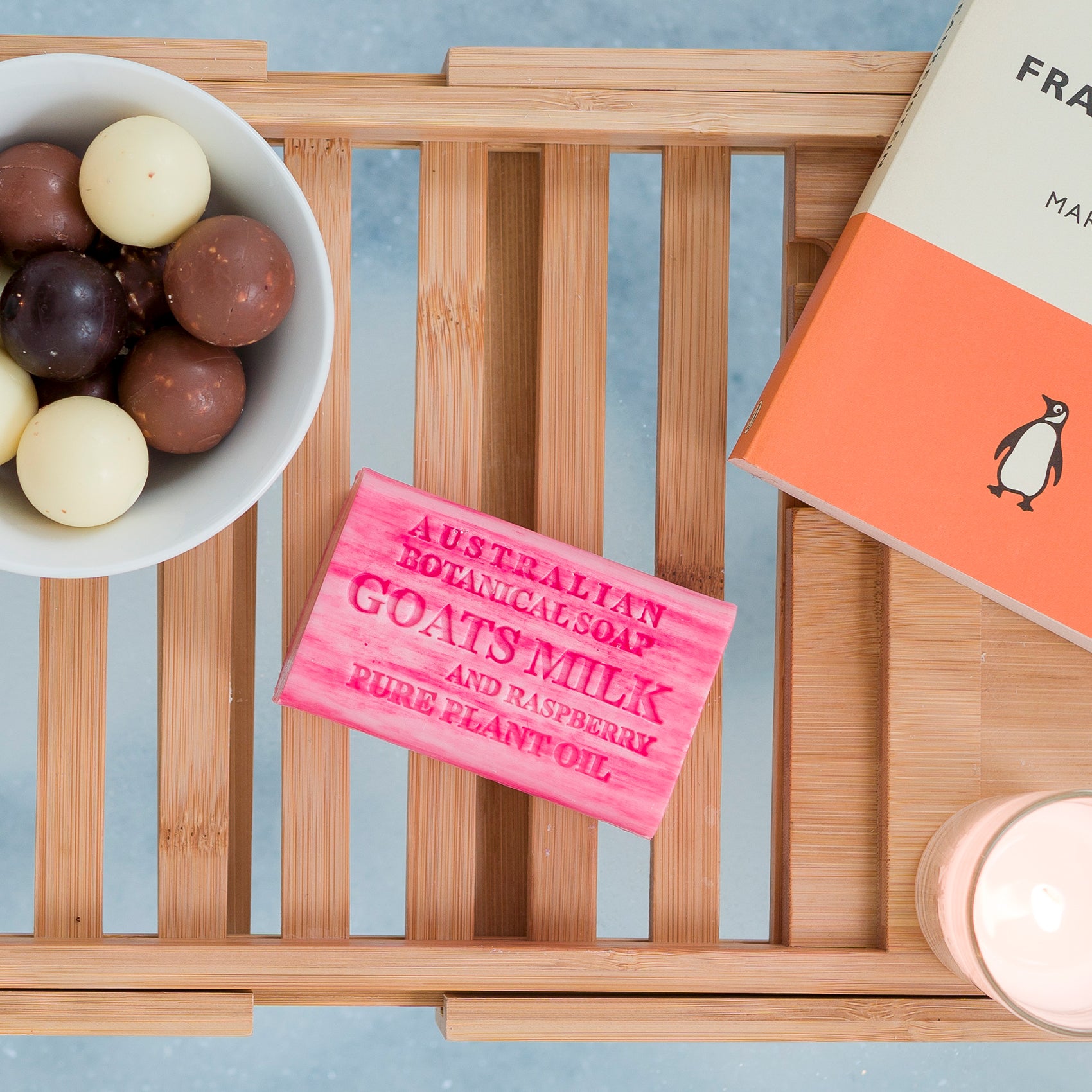 Pink soap bar with text on a wooden tray with a bowl of chocolates and a book.