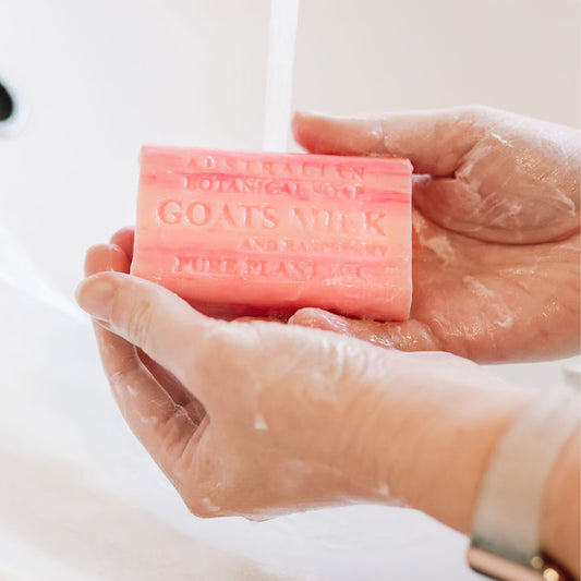 Hand holding a bar of soap with 'Goats Milk' branding against a white background