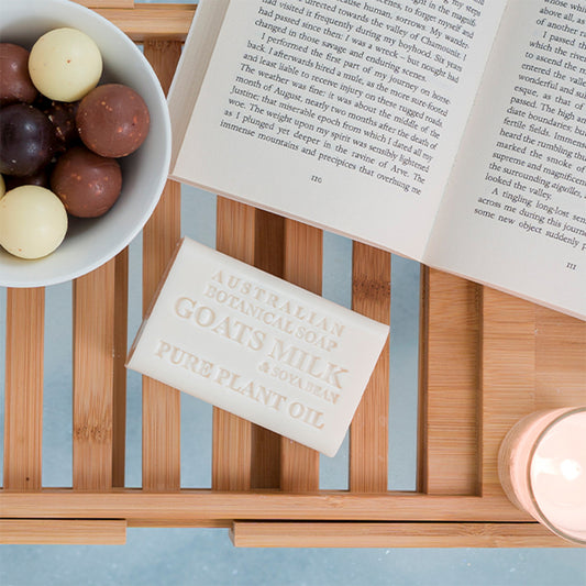 Bowl of chocolates, book, Australian Goats Milk soap bar, and candle on a wooden tray.