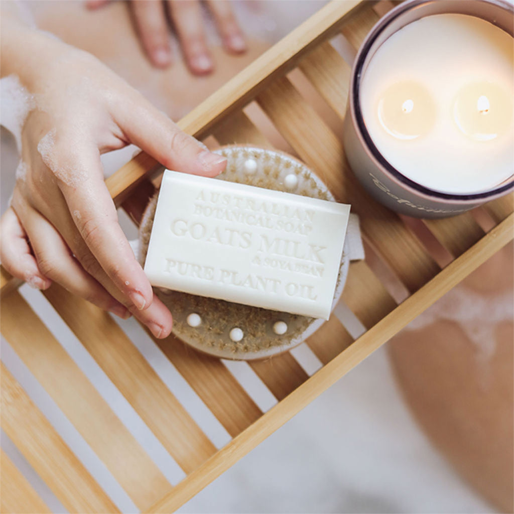 Hand holding a bar of soap on a wooden tray with a lit candle in the background