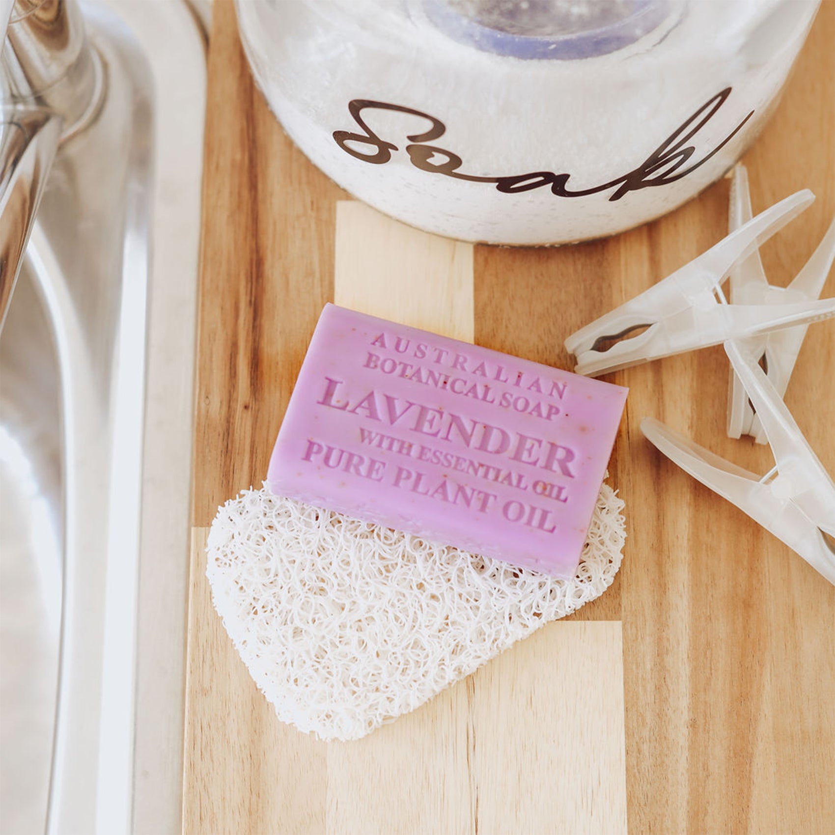 Lavender Soap bar on soap saver pad on wooden counter with bath soaps and clothes pins by a sink