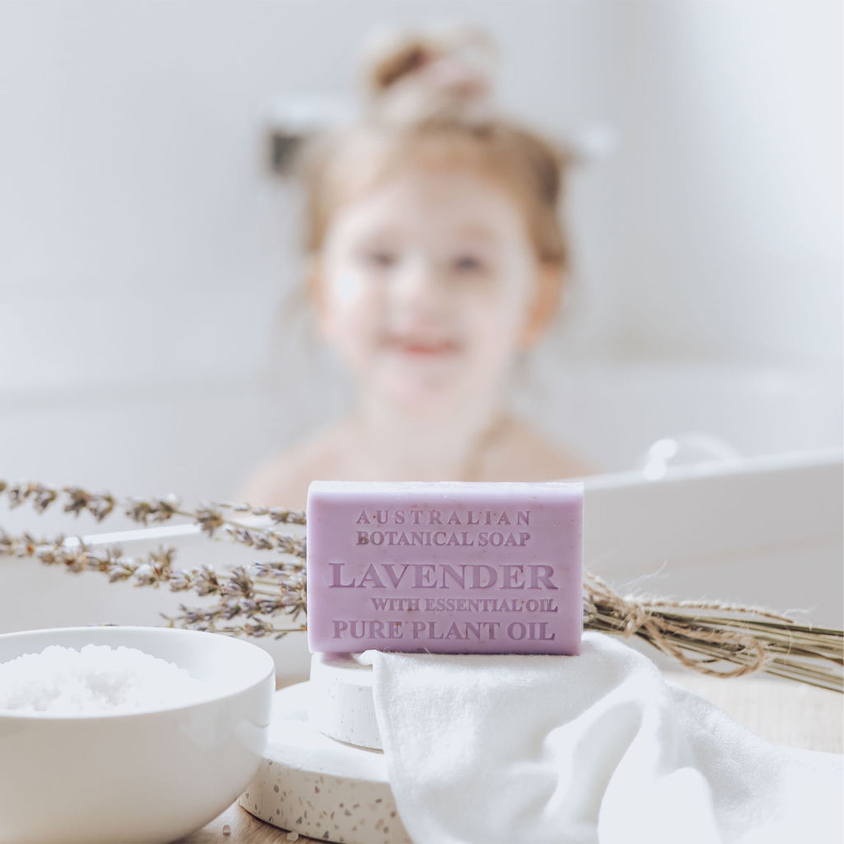 Lavender soap bar with essential oil and plant oil on a white surface with a blurred child in the background.