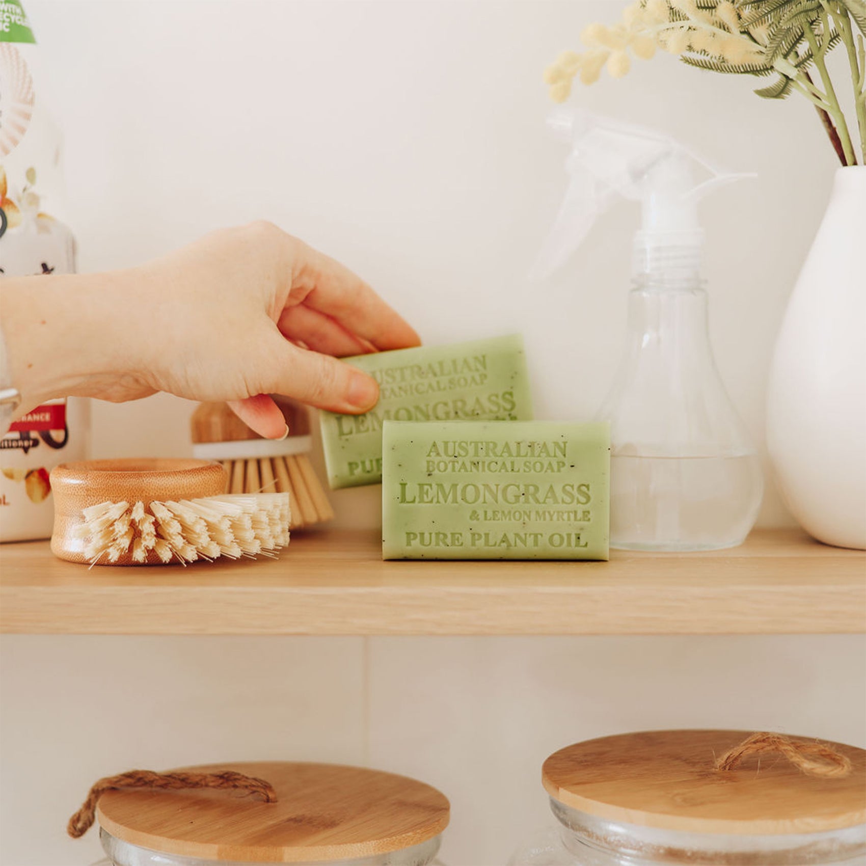 Hand reaching for a bar of soap on a wooden shelf with various items.