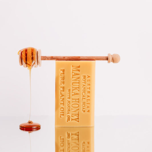 Bar of soap with honey being drizzled over it on a white background
