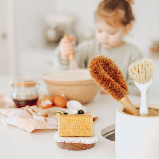 Kitchen counter with cleaning brushes, soap, and a child in the background