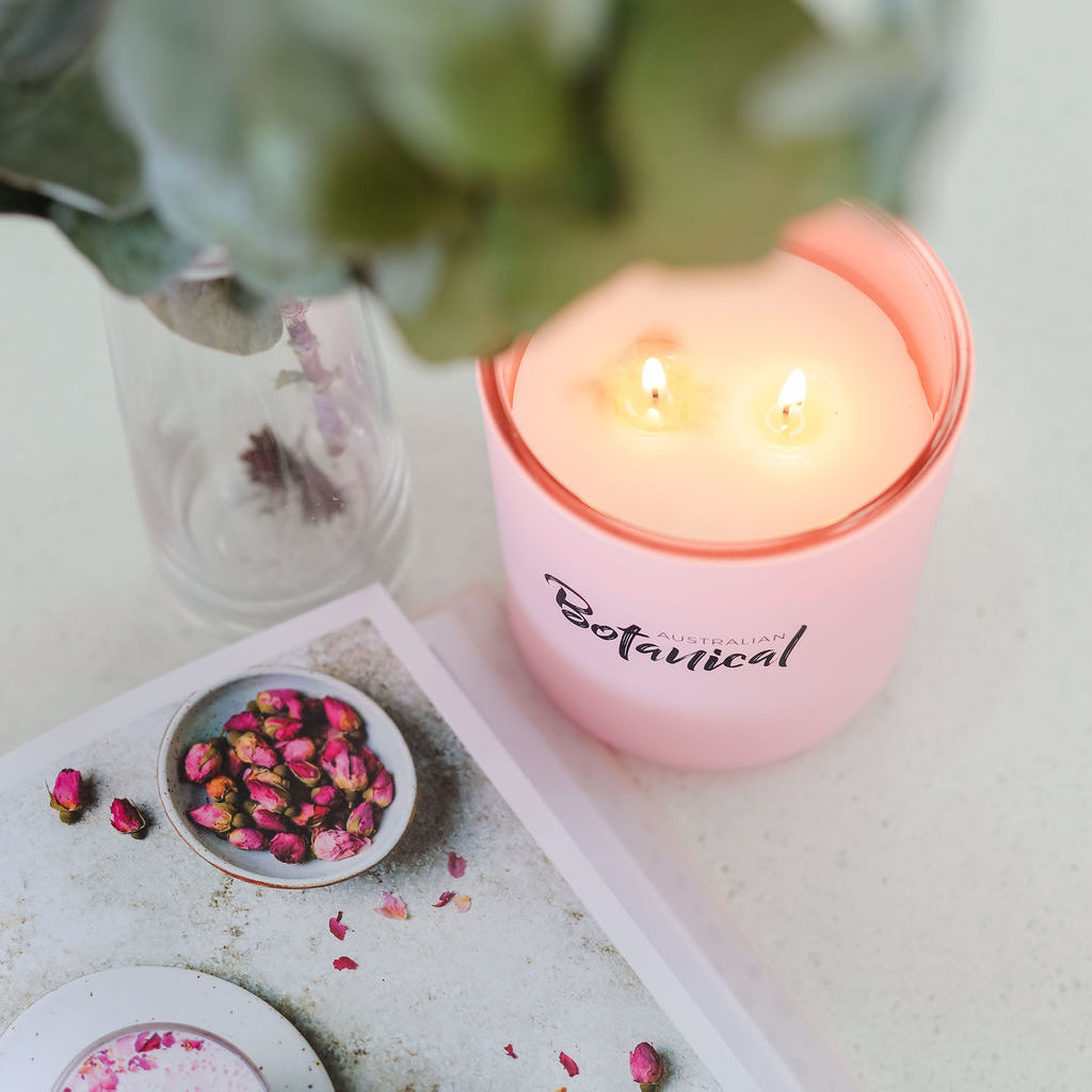 Pink candle labeled 'Botanical' on a surface with dried flowers and a plant in the background