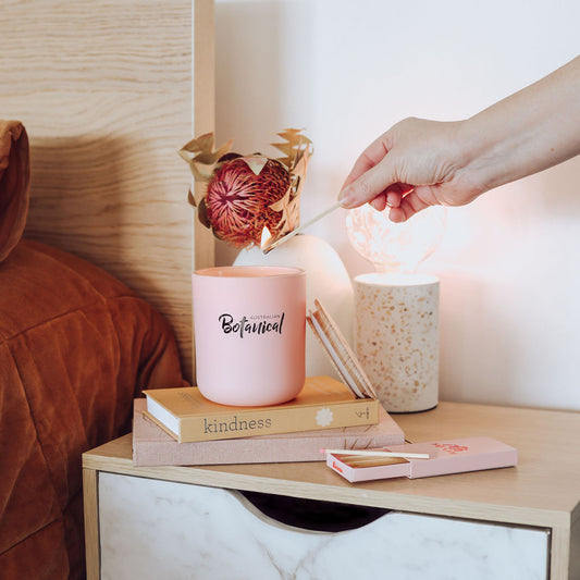 Person lighting a candle on a nightstand with books and decorative items.