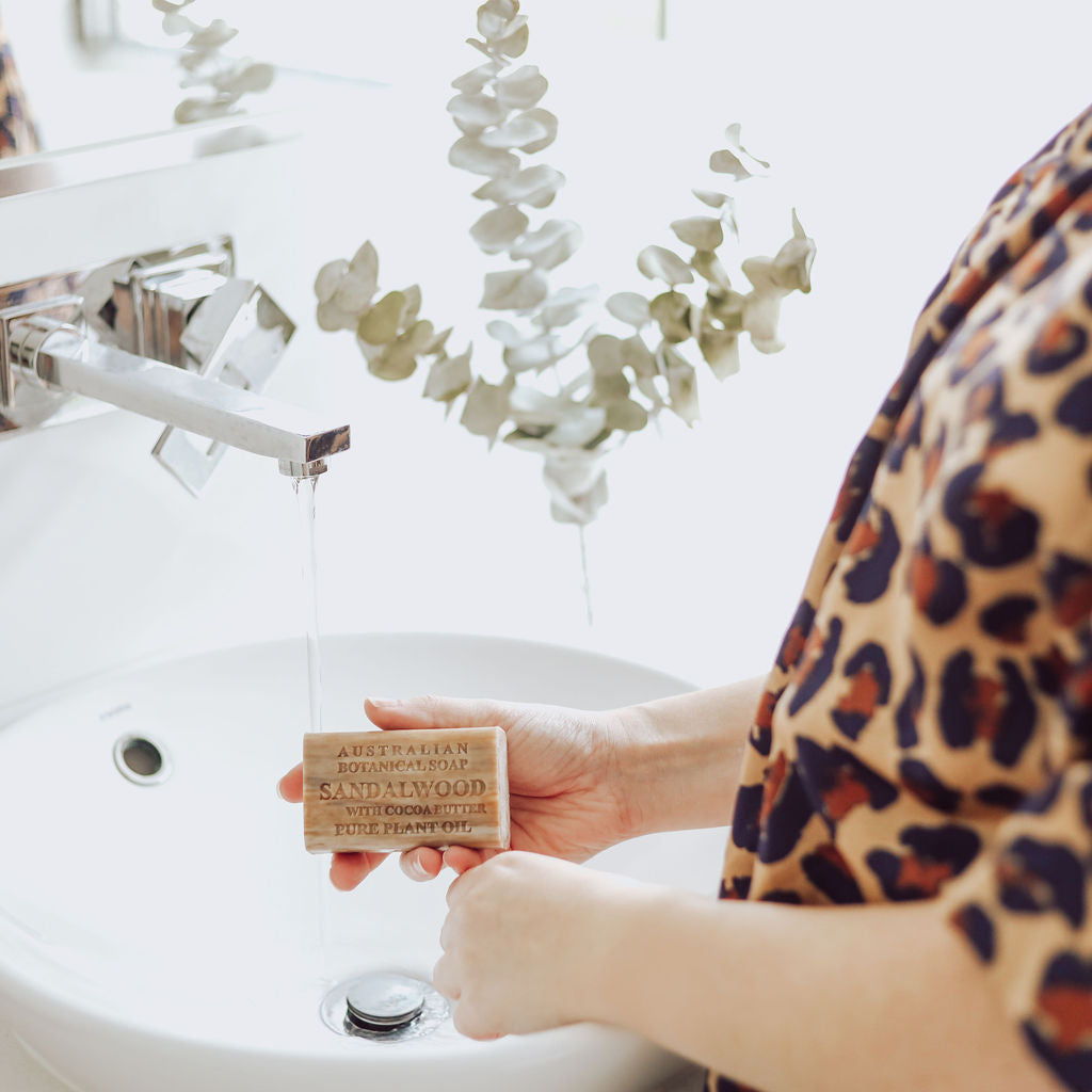 Person holding a bar of soap labeled 'Sandalwood' over a sink with a leopard print sleeve.