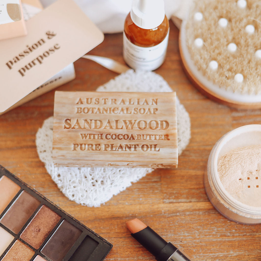 Australian Botanical Soap Sandalwood with Cocoa Butter on a wooden surface with makeup items.
