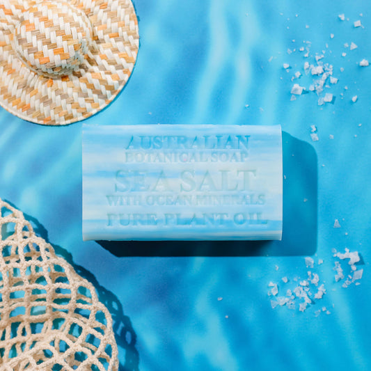 Bar of Australian Botanicals Sea Salt Soap on a blue background with sea salt crystals and a woven hat.