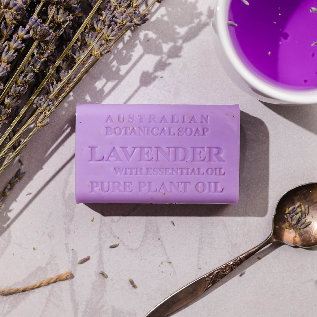 Purple lavender soap bar with essential oil on a textured surface with lavender flowers and a spoon.