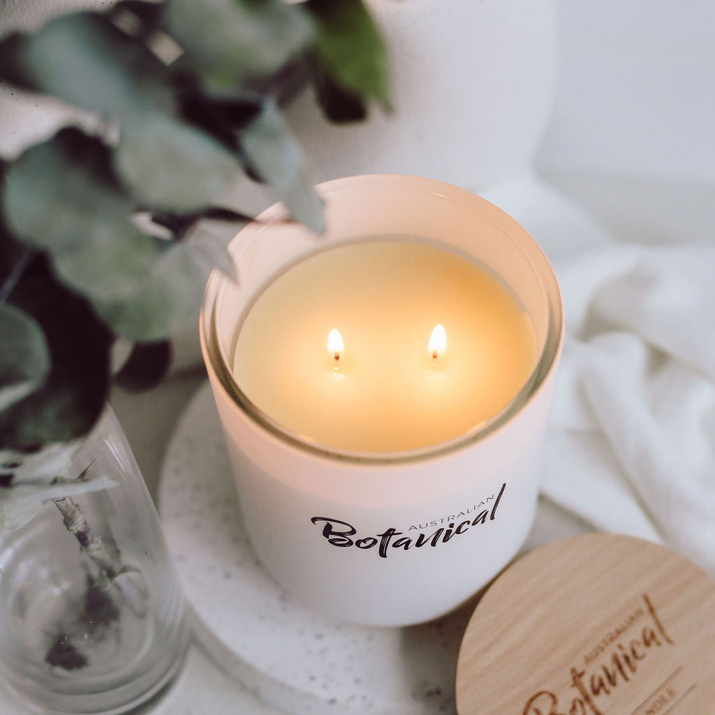 Candle with 'Australian Botanical' branding on a white surface with a plant in the background