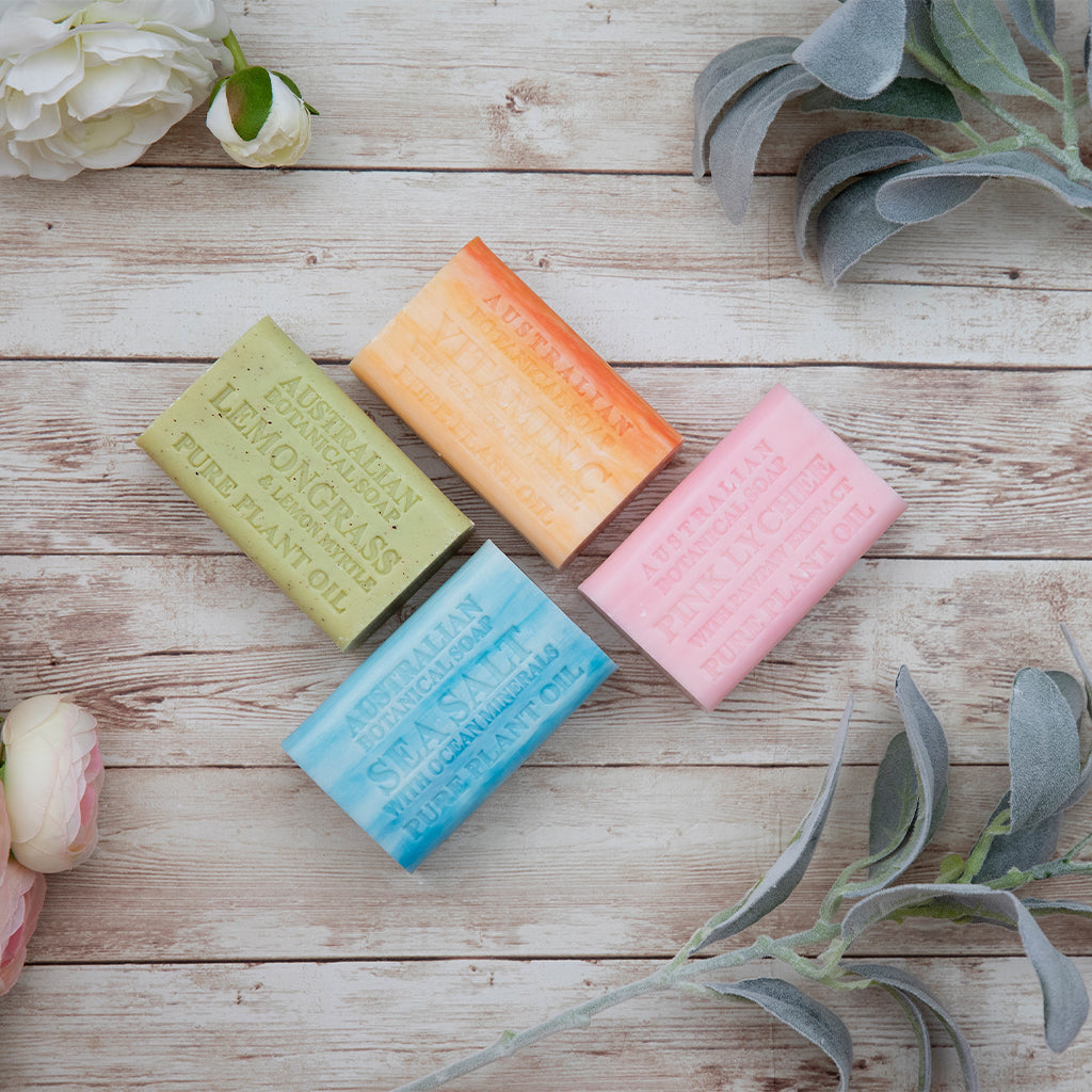 Four colorful soap bars on a wooden surface with flowers and leaves.