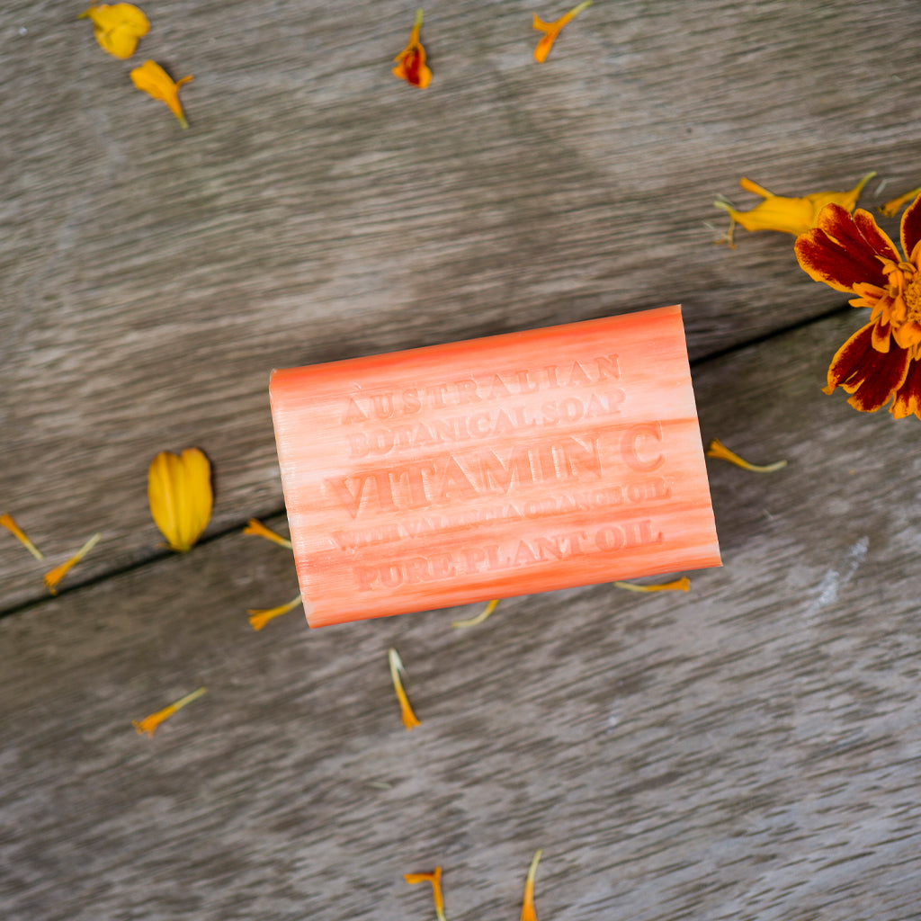 Bar of soap with 'Vitamin' embossed on a wooden surface with flowers.