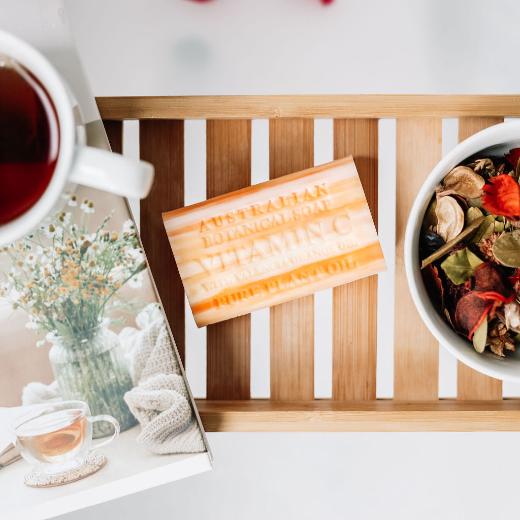 Tea cup, soap bar, and bowl of tea leaves on a wooden tray with a white background
