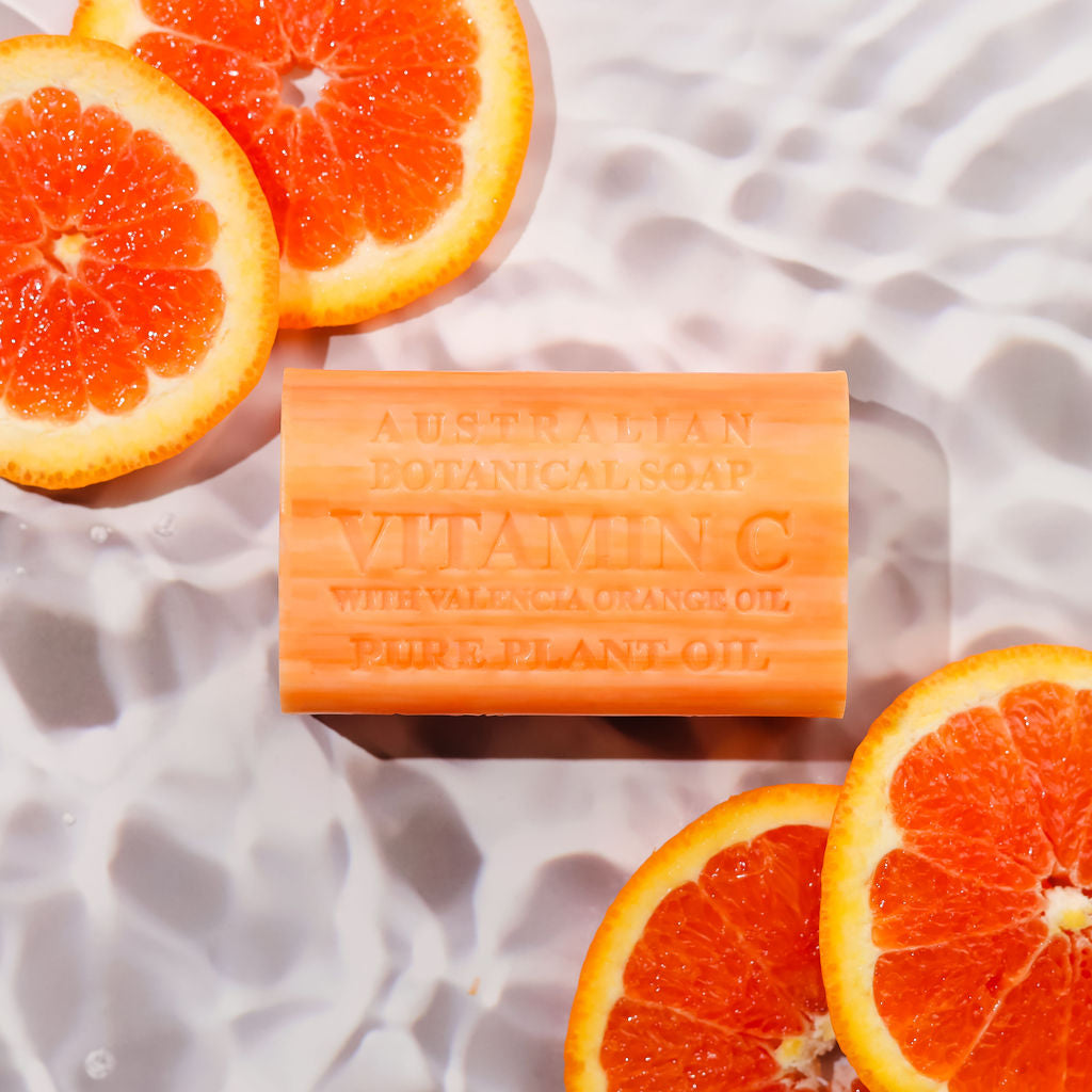 Bar of Australian Botanical Soap with Vitamin C surrounded by sliced oranges on a textured white surface.