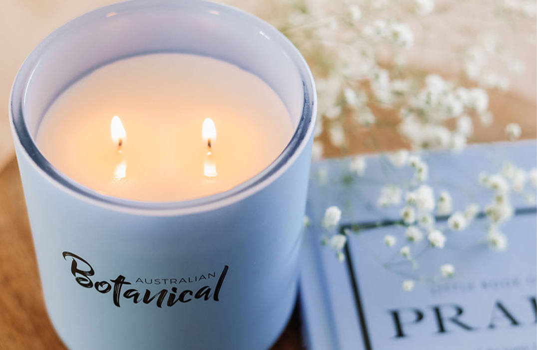 Aqua Escape Soy Candle on table with twin wicks lit with white flowers and book